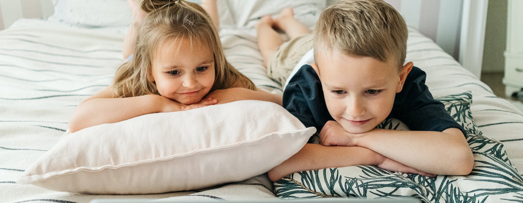 Two Young Kids Laying On Bed With Laptop